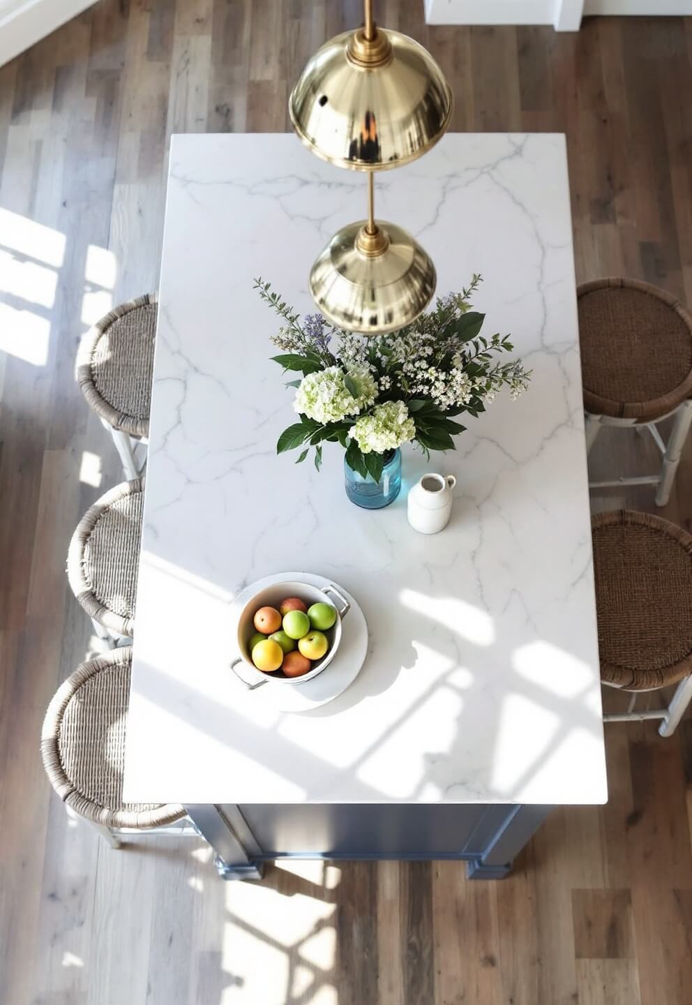 Overhead view of a navy blue farmhouse kitchen island during breakfast with quartzite top, seagrass barstools, white ceramic fruit bowl, vintage mason jar with hydrangeas, and pendant lights.