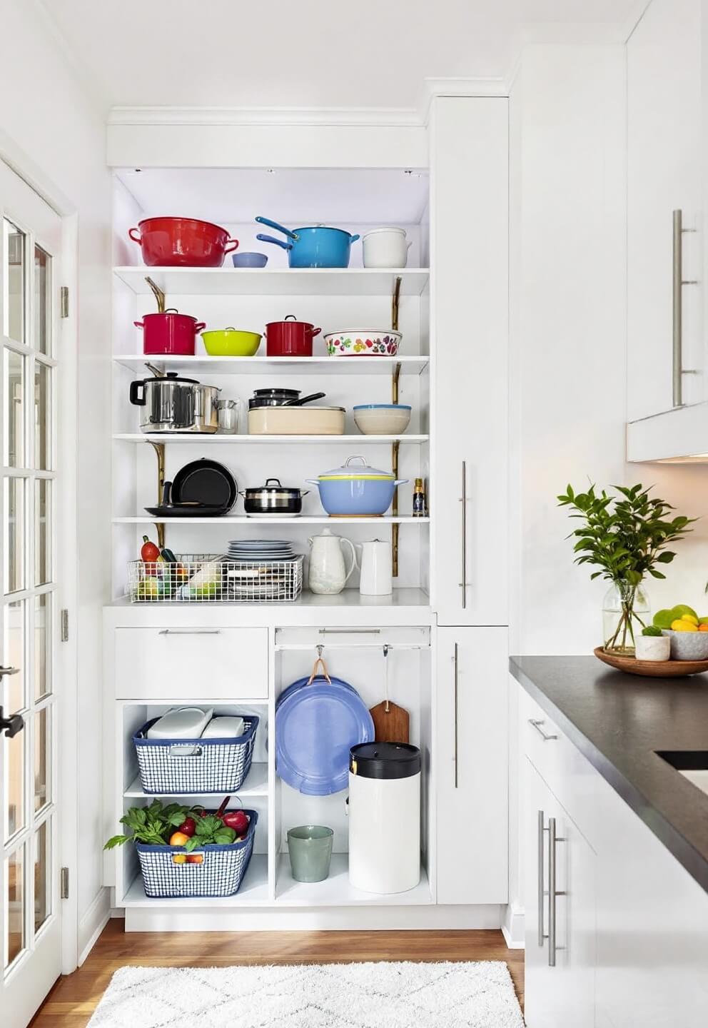 Smartly designed contemporary micro-kitchen with illuminated open shelves presenting colorful cookware and under-cabinet baskets with fresh produce, showcasing a clever use of vertical space