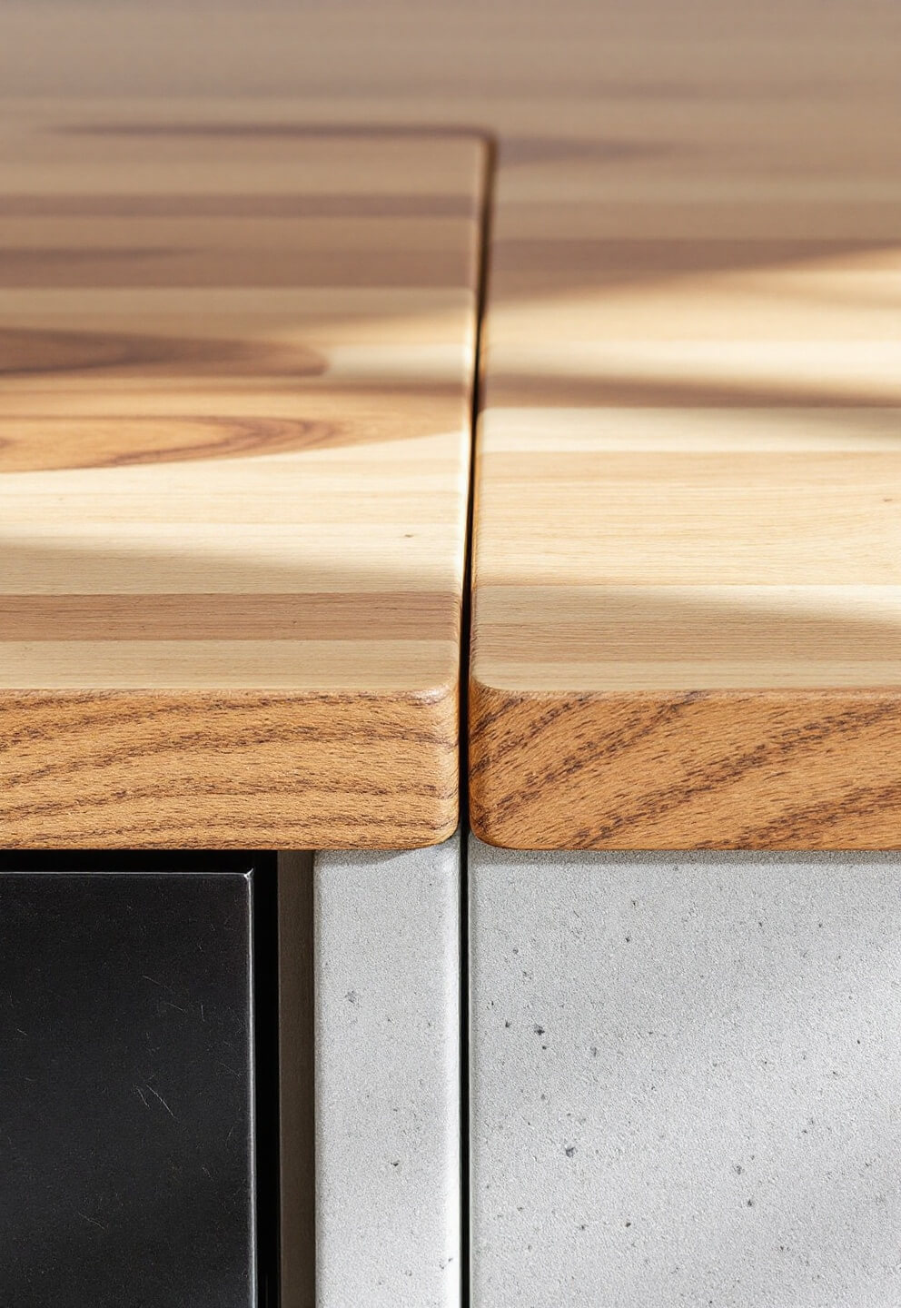 High-quality barndo kitchen showcasing the precise junction of butcher block and brushed steel, warm wood with cool concrete in natural light, captured at f/4 for selective focus with minimal styling.