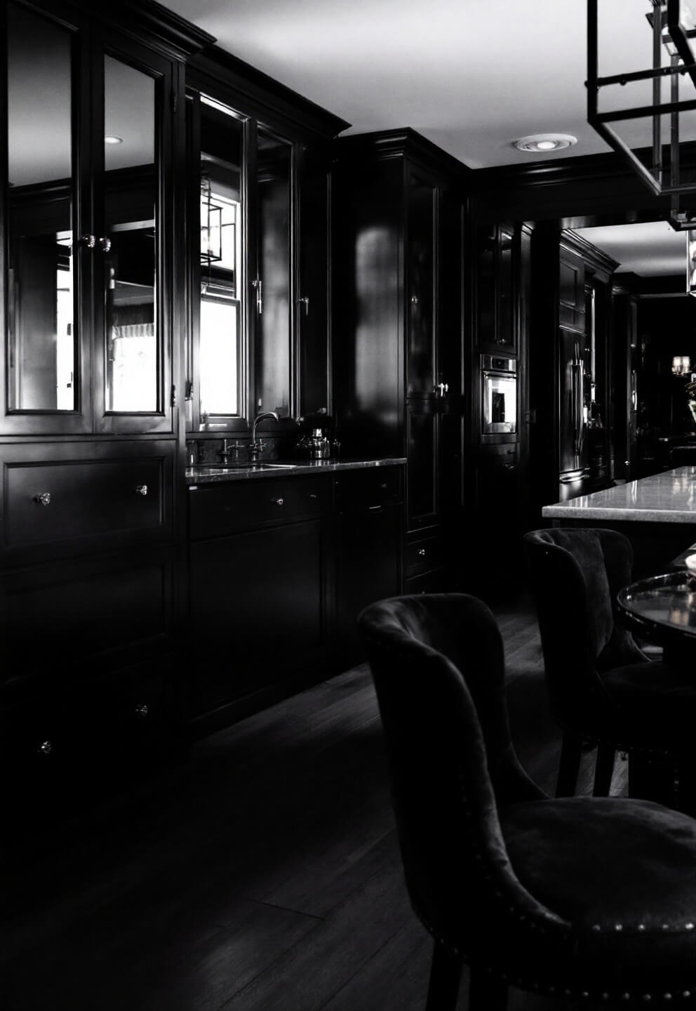 Vintage-style black kitchen with satin and gloss cabinets, soapstone counters, antique mirrors, and velvet bar stools under evening lighting.