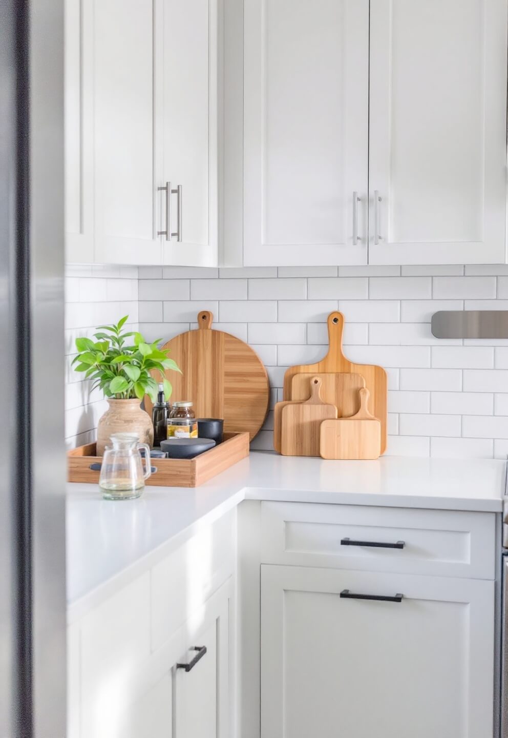 Compact, clean L-shaped kitchen with white counters, bamboo cutting boards, and sleek organizing trays illuminated by morning light.