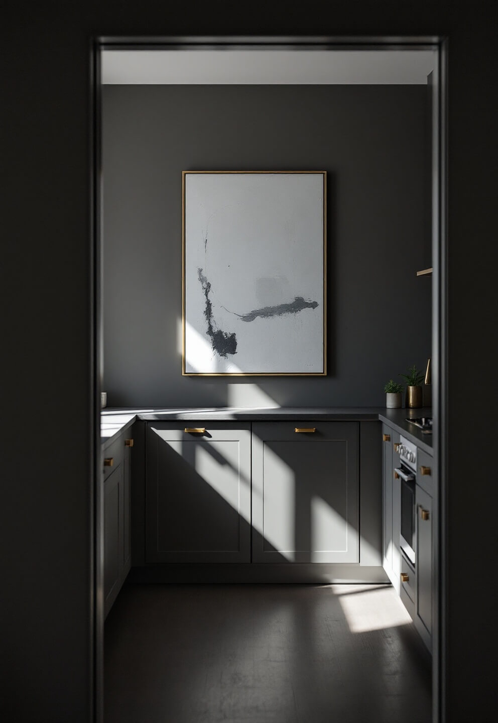 Minimalist gray kitchen with brass accents, highlighted by an oversized abstract canvas artwork, seen through a doorway frame in late afternoon light casting dramatic shadows.