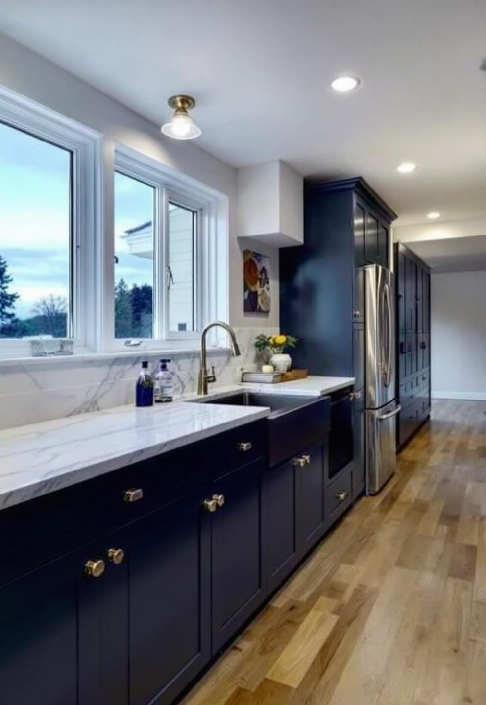 Transitional galley kitchen at dusk featuring navy blue cabinets with polished nickel hardware, Calacatta marble countertops and backsplash, raised ceiling detail, and organized deep drawers, shot at f/2.0 for a mood-lit effect.