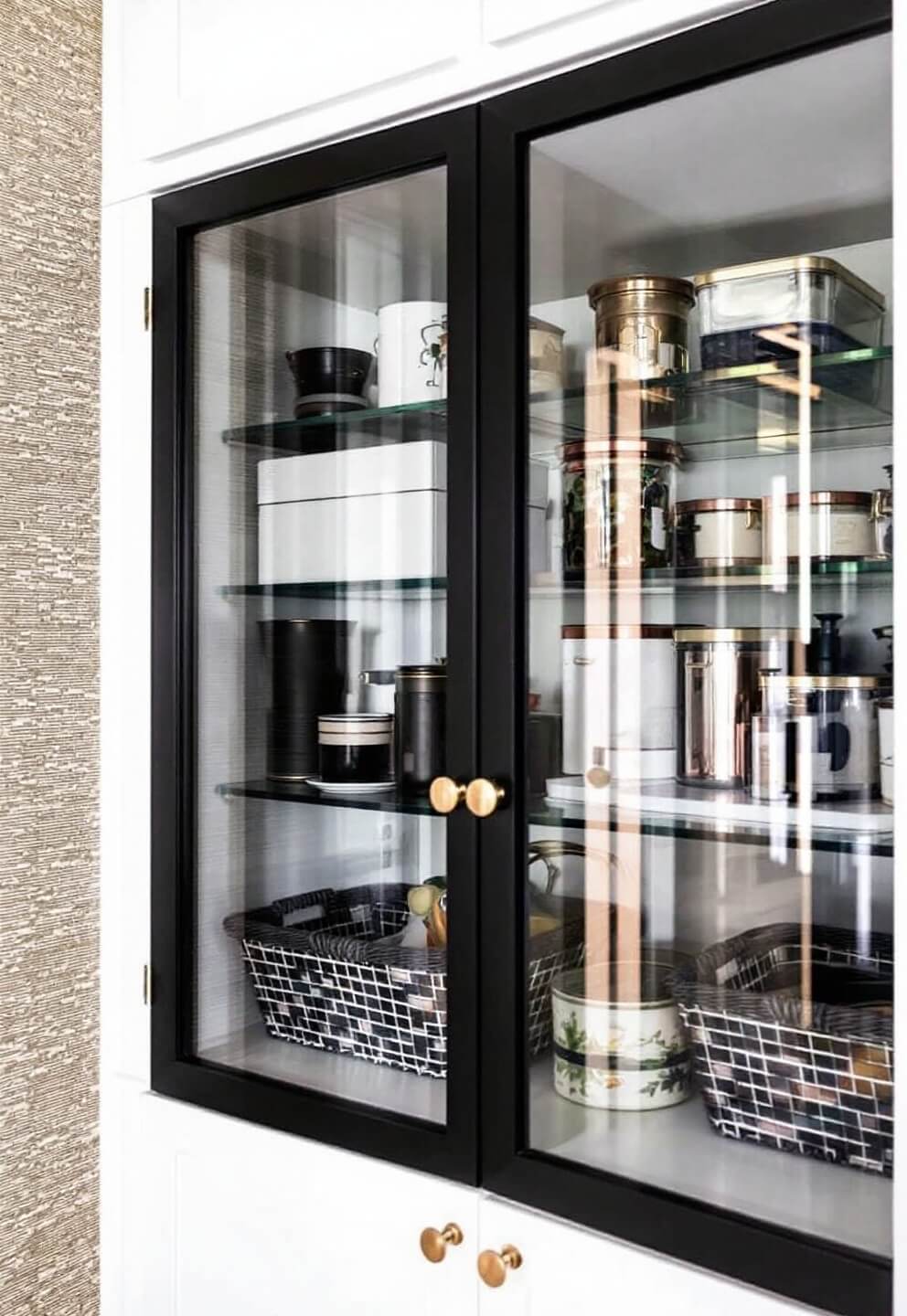 Modern pantry with glass-front cabinet, organized storage containers, copper and brass accents in bright daylight.