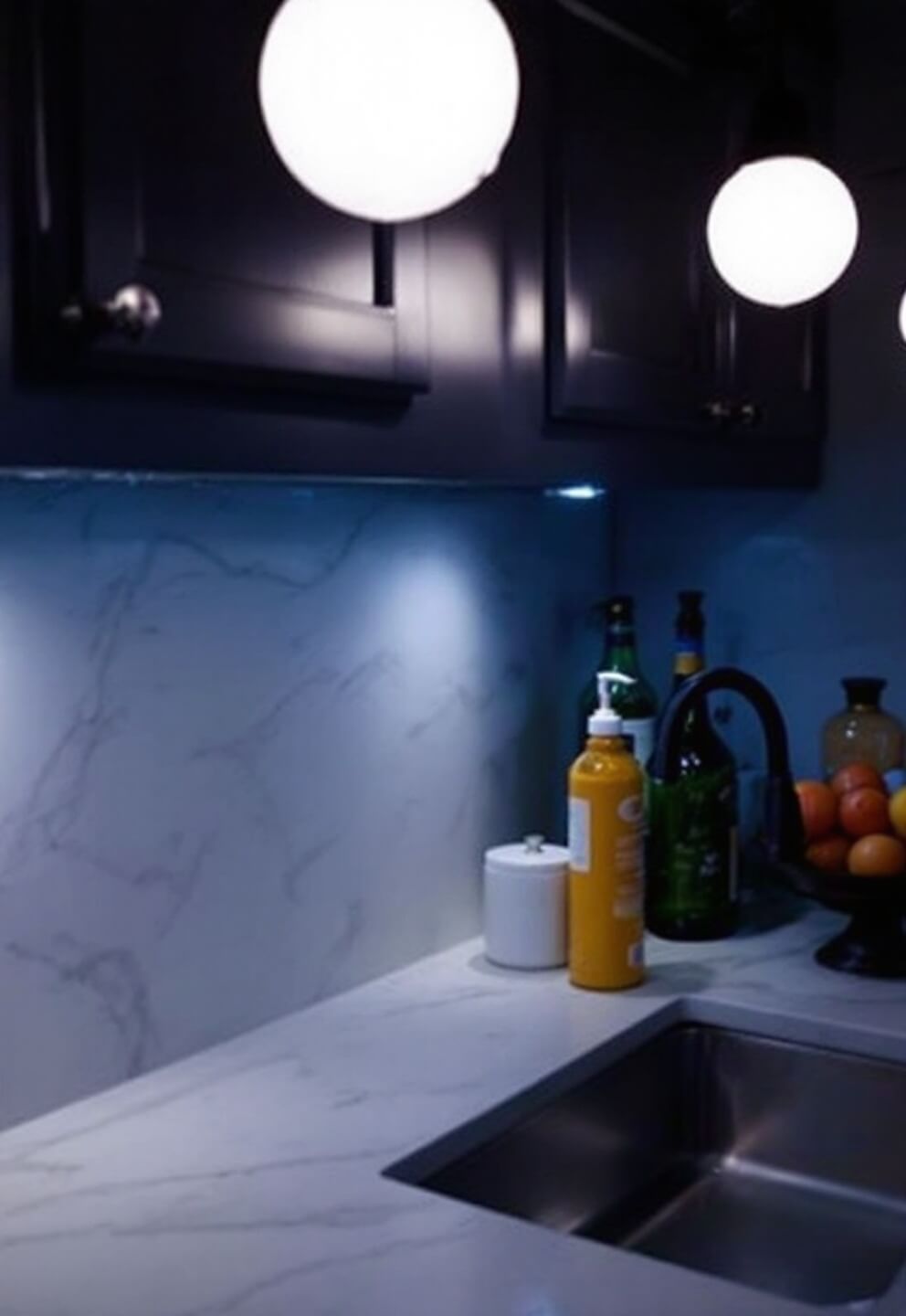 Evening kitchen scene featuring layered lighting, illuminated quartz countertops, glass globe pendants, and a matte black faucet as a focal point.