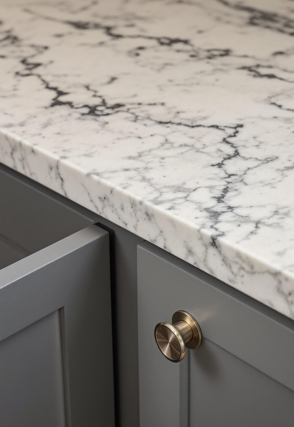 Close-up of matte-finished kitchen cabinet with brushed steel handles and veined quartz surfaces under ring light at midday