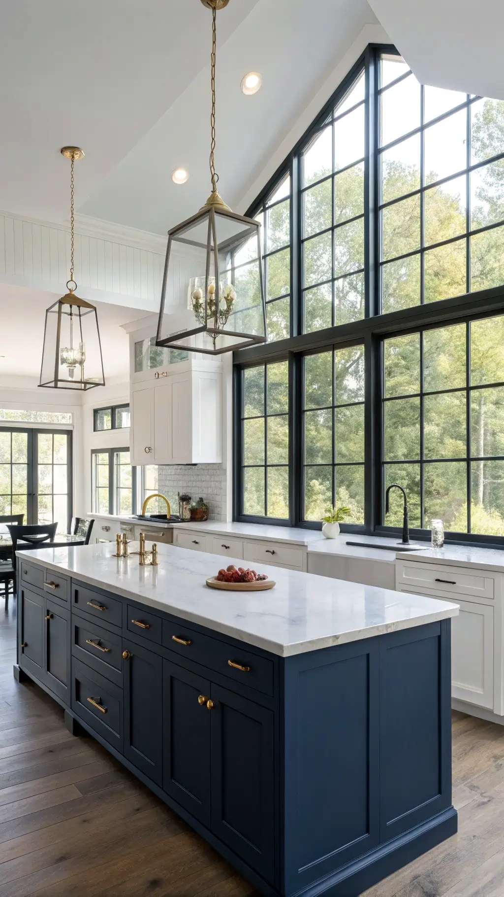 Bright, open-concept kitchen with contrasting navy blue island and white cabinets, double-height windows with black frames, and smokey glass pendant lights captured from the dining area at midday.